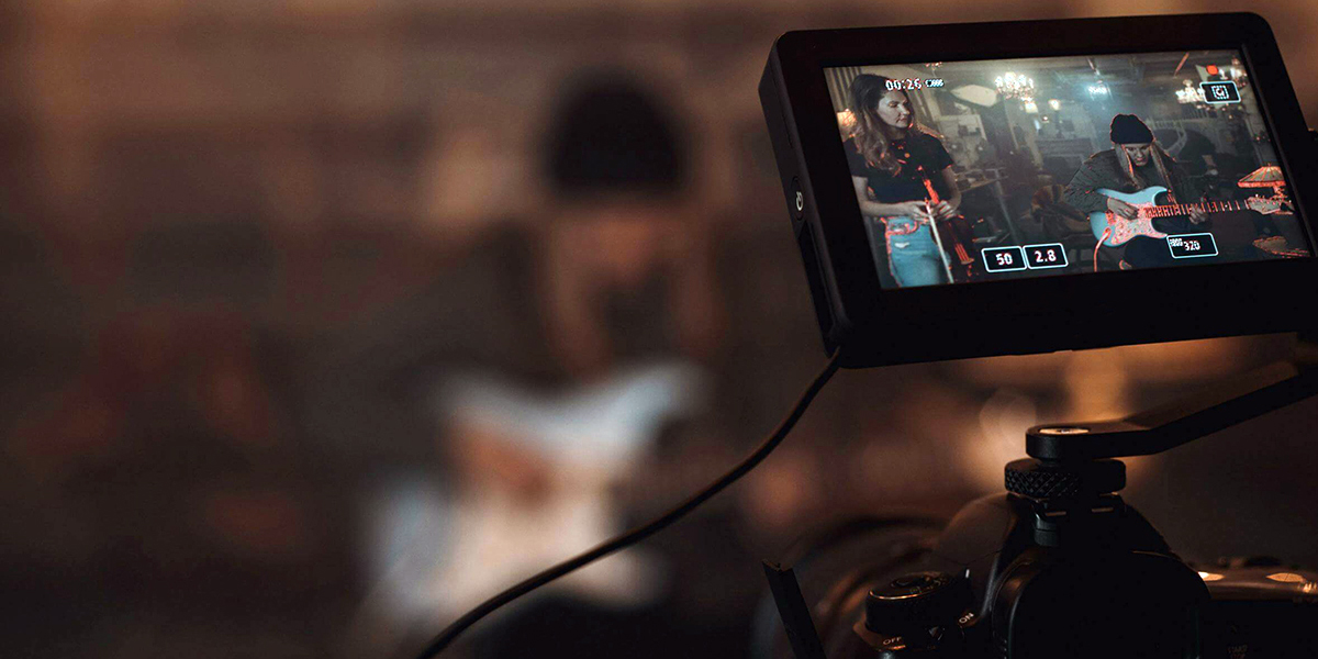 Monitor screen on camera showing two musicians with guitars in a dimly lit setting.