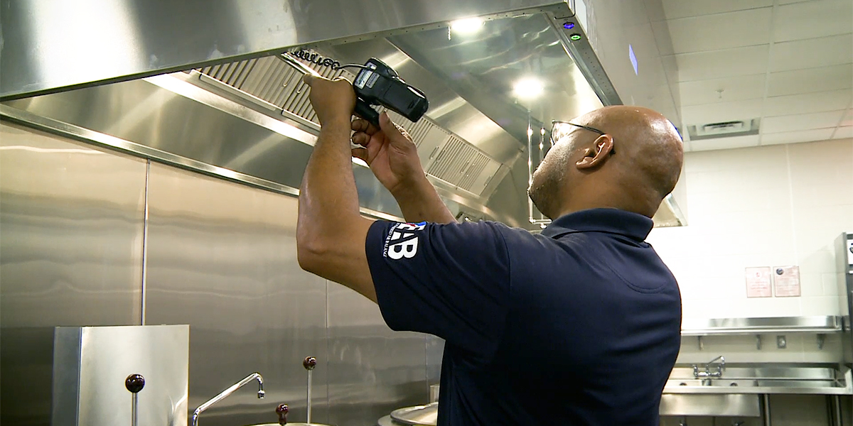 A person in a dark shirt with "eab" on the sleeve works with a tool to fix or install a component in an aabc commercial kitchen exhaust hood system.