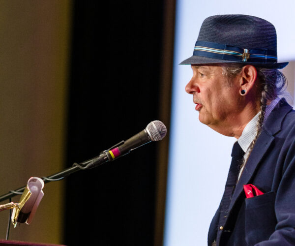 Man in hat speaking at conference podium
