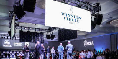 Attendees gathered indoors beneath a decorative event sign with sponsor logos on display.