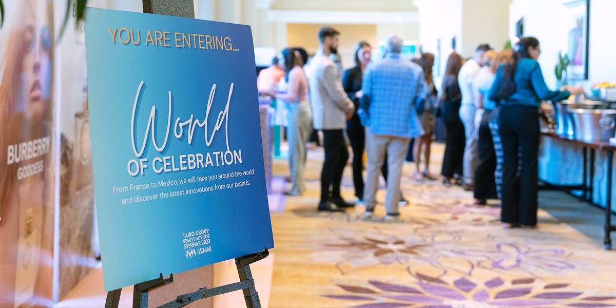 A sign reads "world of celebration" at an event at jw marriott orlando, grande lakes with people gathered and chatting in the background.