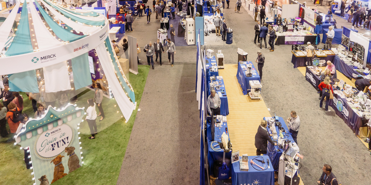 The bustling trade show floor at the orange county convention center features various booths, including a carousel-themed section on the left, with attendees eagerly interacting with exhibitors and products at vmx.