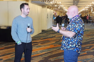 Two men speaking during an interview in a conference hallway.