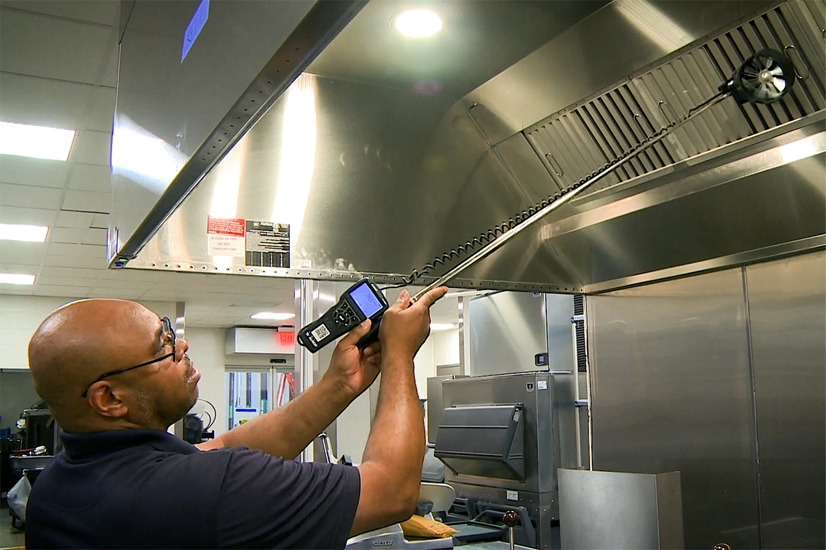 Technician measuring kitchen hood ventilation airflow.