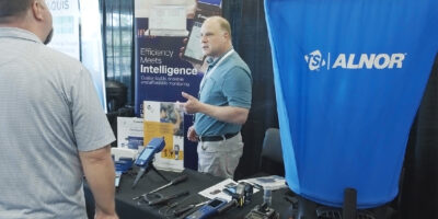 Two people talking at an equipment trade show booth with instruments displayed on the table.