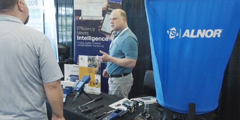 Two people talking at an equipment trade show booth with instruments displayed on the table.