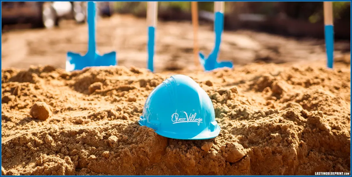 Blue construction helmet on sandy ground with shovels.