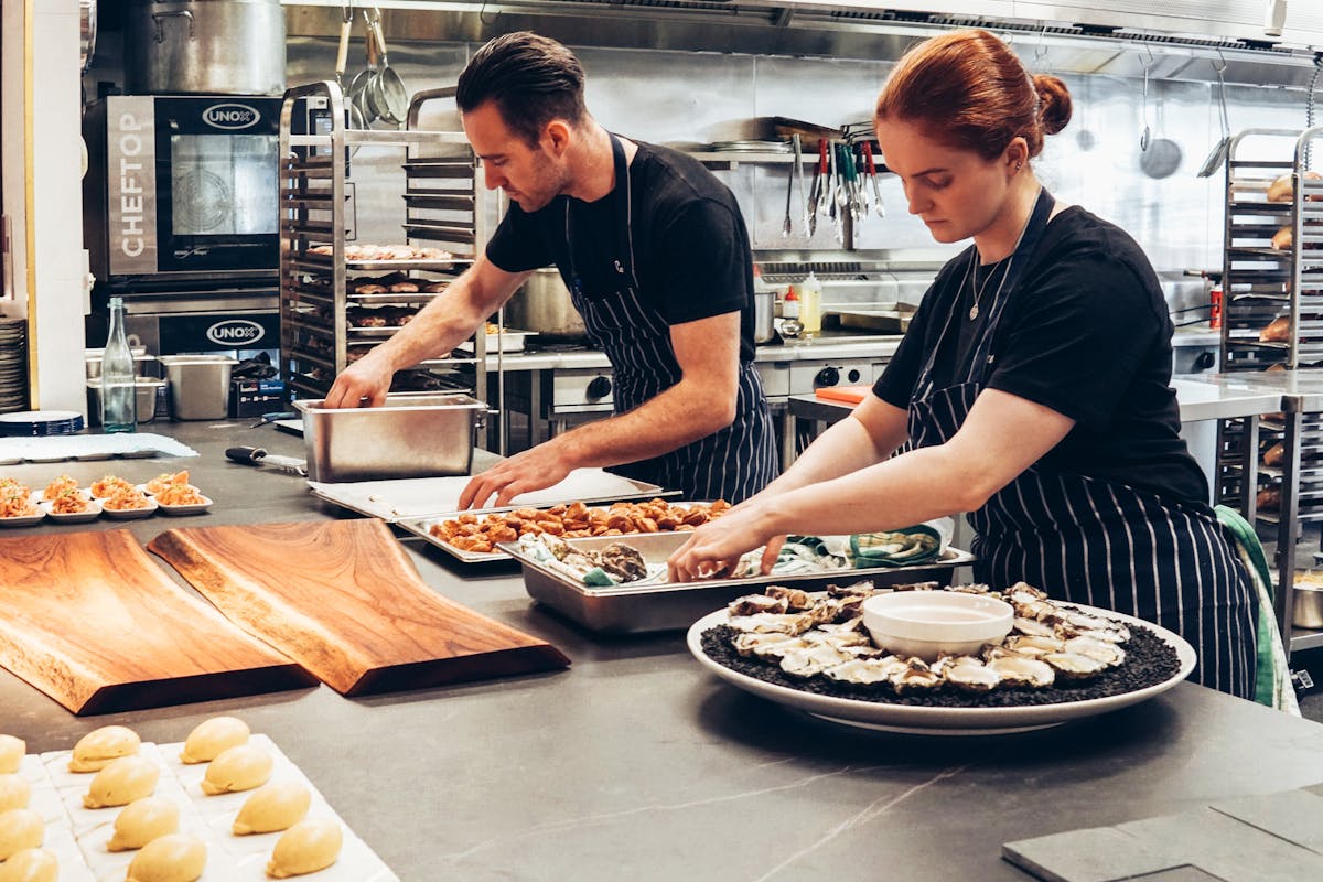 Man and woman wearing black and white striped aprons cooking