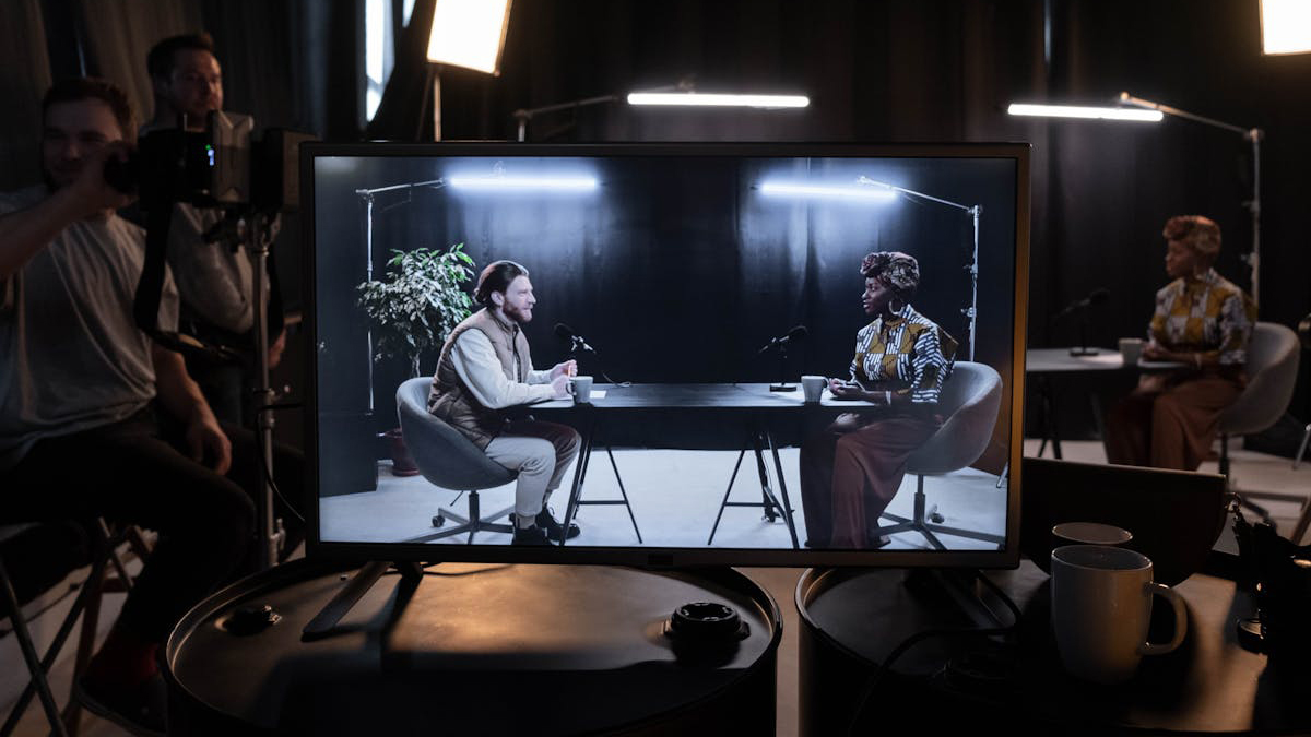 Two people sit across from each other at a table in orlando, deep in conversation. On a monitor, the scene highlights what are video production services, with crew and lighting gear subtly visible.