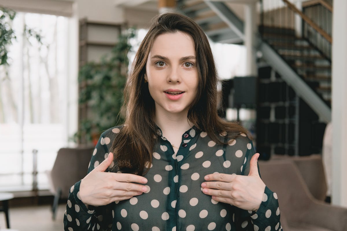 A woman with long hair, wearing a polka dot blouse, gestures passionately in a room with a staircase and plants, suggesting an elegant setting for an orlando nonprofit video production.