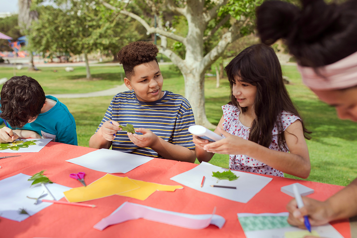 Children outdoors, happily working on an art project with paper, glue, and leaves. Storytelling is is one of the types of nonprofit videos.