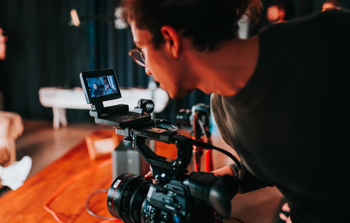 A videographer expertly operates a video camera indoors, honing their craft by focusing on a screen that displays the captured image from the lens.