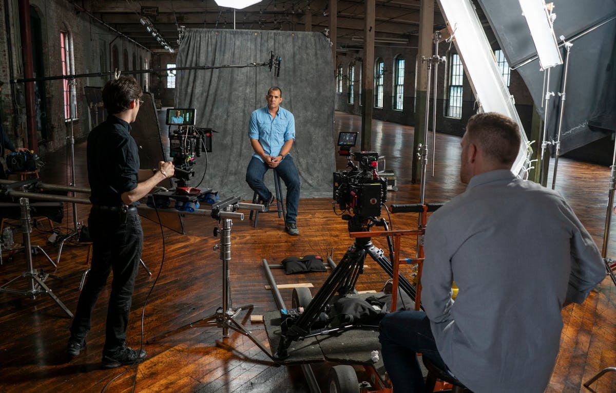 Seated for a video interview in a spacious studio, the person is surrounded by professional lighting and equipment, expertly managed by two crew members, reflecting top-tier orlando video production standards.