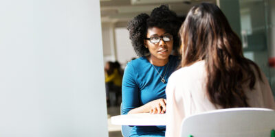 Two people talking across a table in a bright office.
