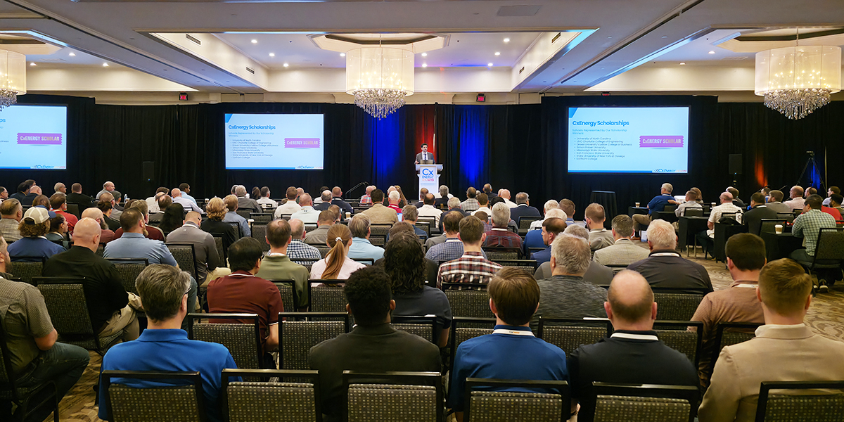 Full audience view of the cxenergy 2025 keynote session on scholarships, with speaker at the podium and two presentation screens.