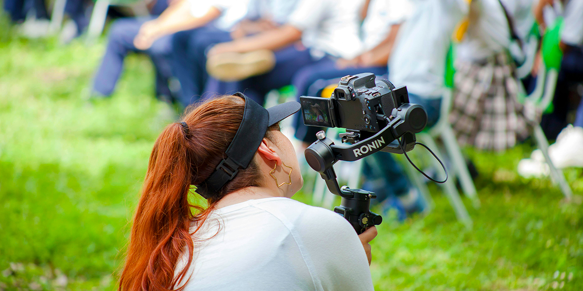 Female videographer filming an outdoor school event with children seated in the background — hiring an event videographer in orlando.