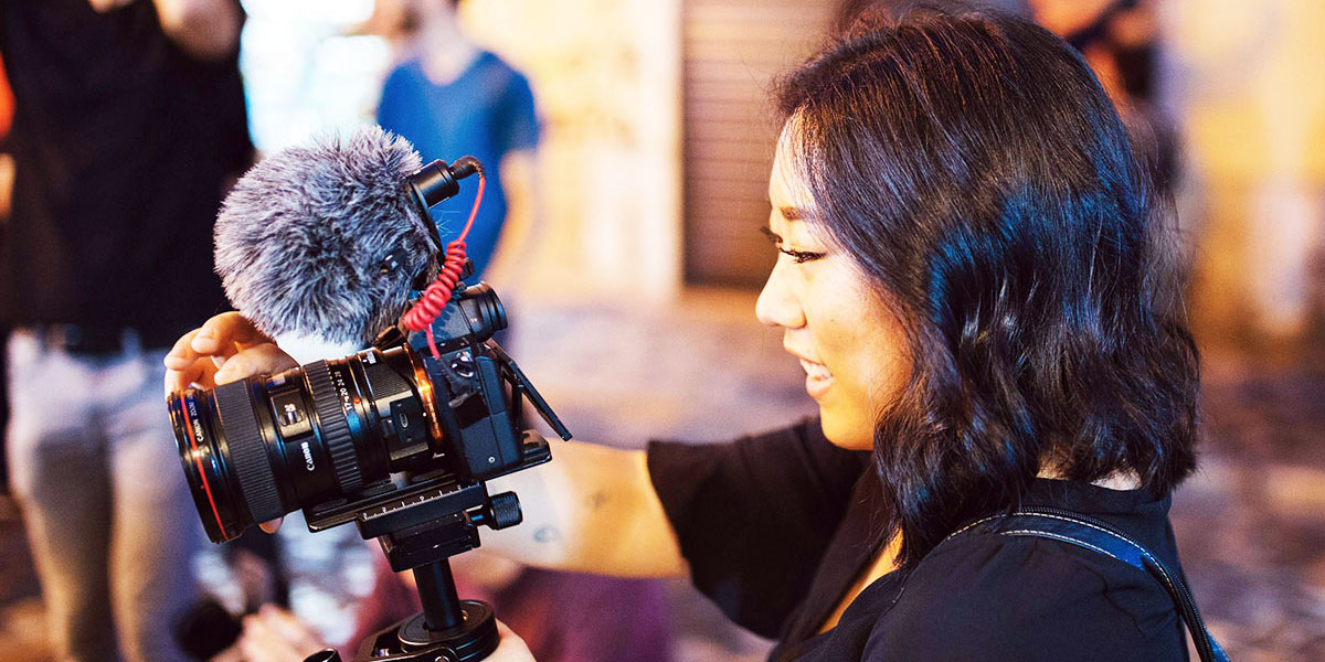 Videographer recording video with a handheld camera and external microphone during a live shoot
