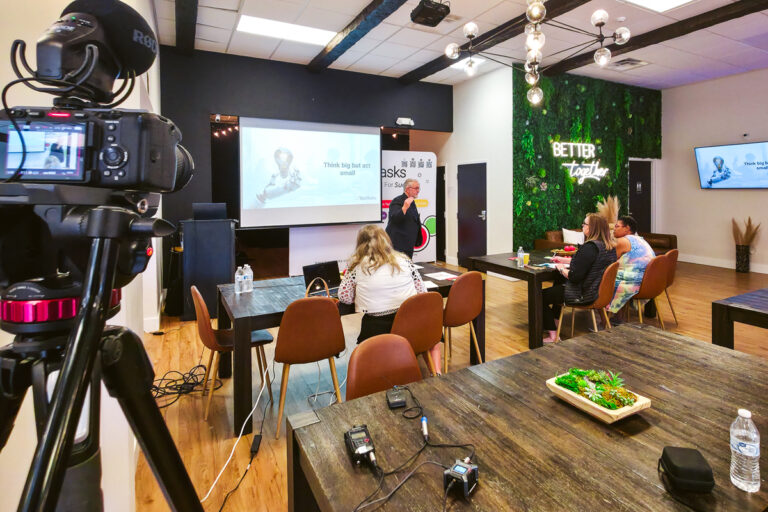 Camera filming a presenter during an Orlando business event with attendees seated in the room.