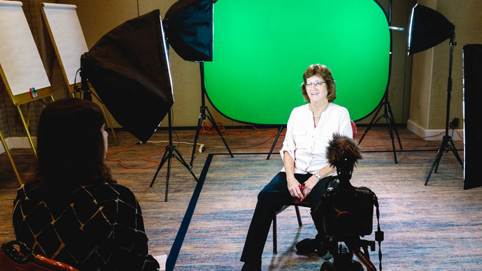 Woman giving a customer testimonial in front of green screen background.